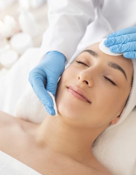 Facial Care. Cosmetologist Using Cotton Pads, Cleansing Skin Of Young Indian Woman During Beauty Treatments In Salon, Relaxed Hindu Female Lying On Table With Closed Eyes, Enjoying Skincare Procedure