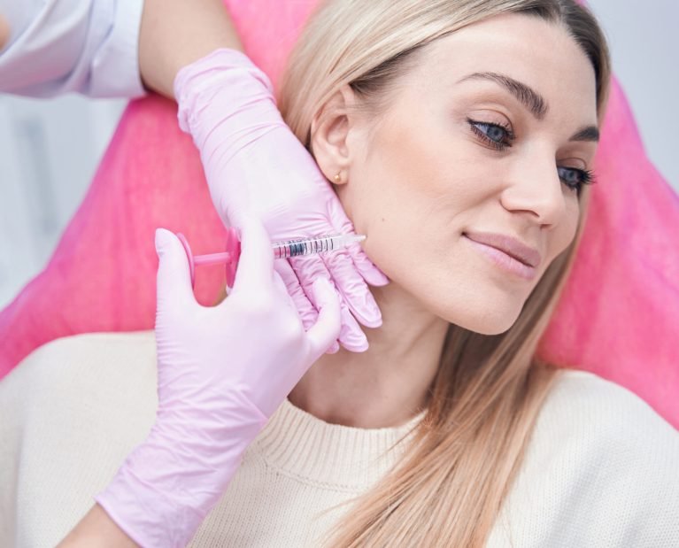 Smiling tranquil young woman daydreaming during mesotherapy procedure performed by experienced cosmetician